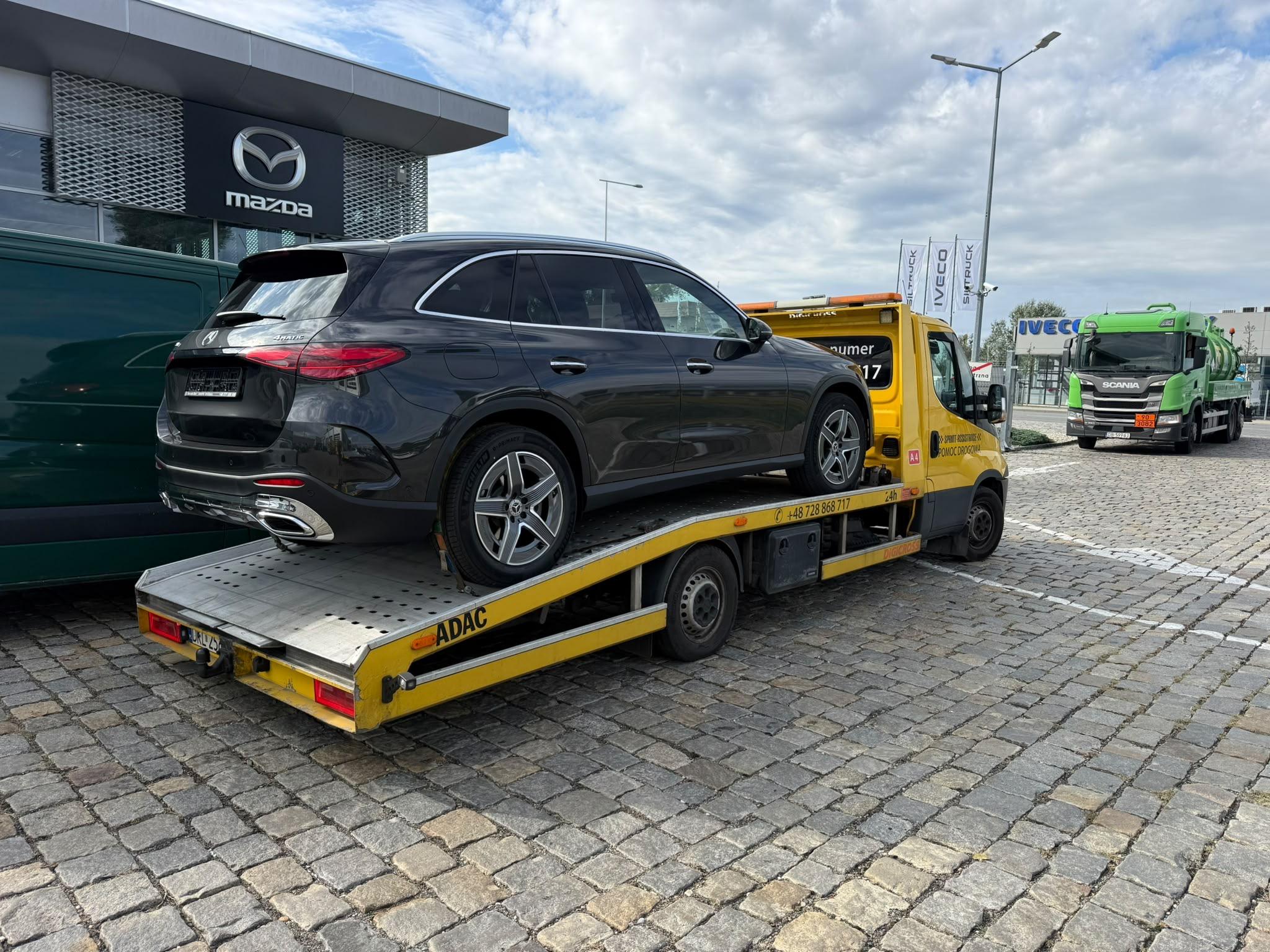 Laweta z czarnym SUV-em Mercedes na platformie przed salonem samochodowym