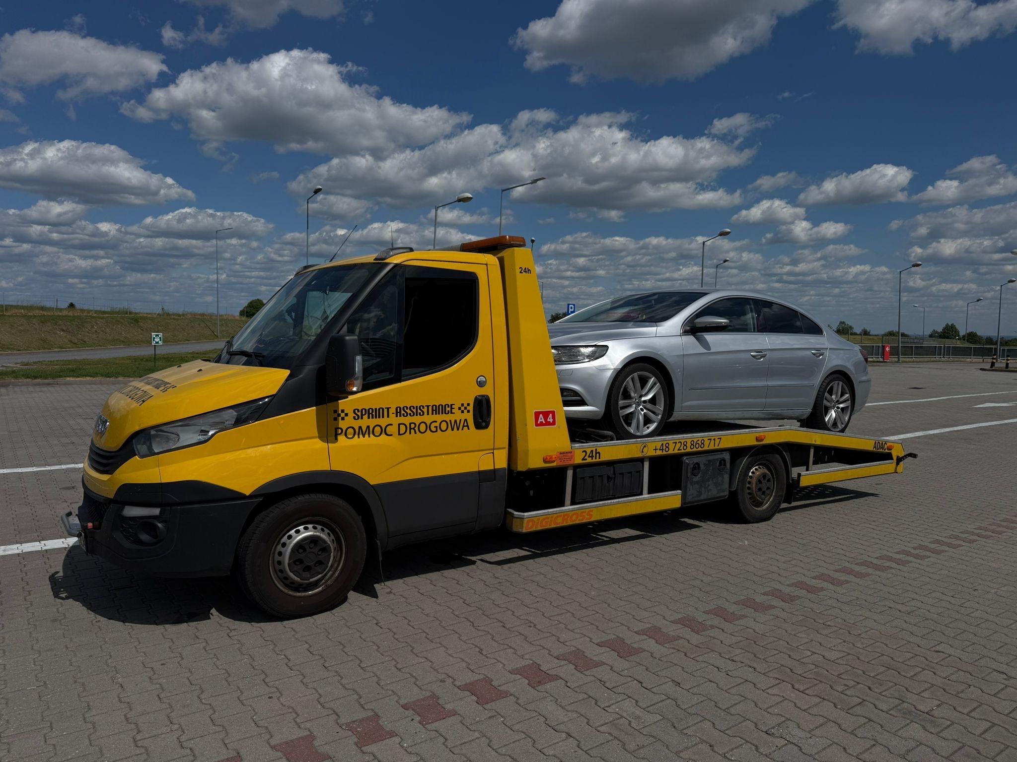 Laweta ze srebrnym sedanem na platformie na parkingu