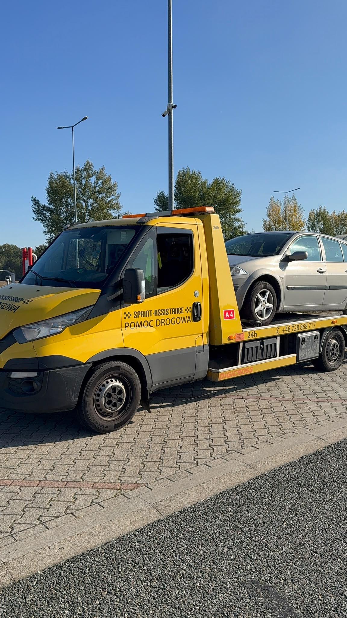 Laweta ze srebrnym autem osobowym na platformie na parkingu