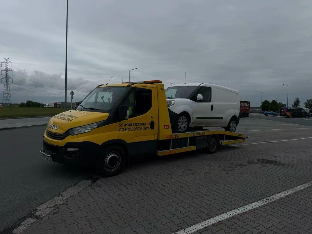 Laweta z białym samochodem dostawczym na platformie na parkingu